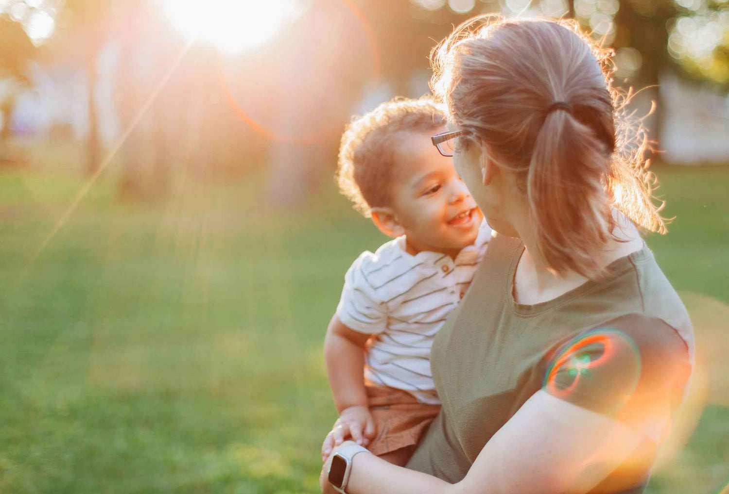 Woman holding a child in a park with a warm, blurred background